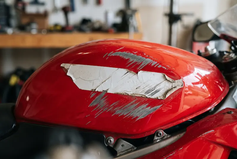 Close-up of gray scrape marks and a cracked, peeling decal on a red motorcycle fuel tank